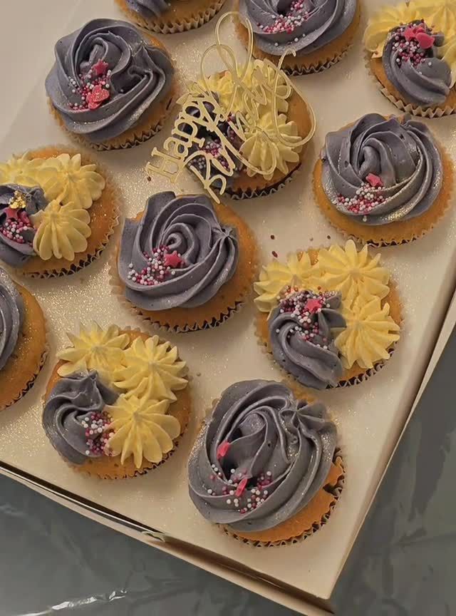 A box of grey and yellow cupcakes with a gold Happy Birthday topper
