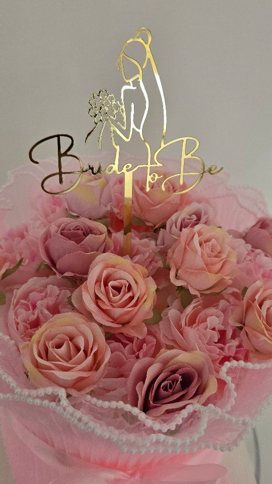 A pink bridal cake topped with fresh roses and a gold Bride To Be topper