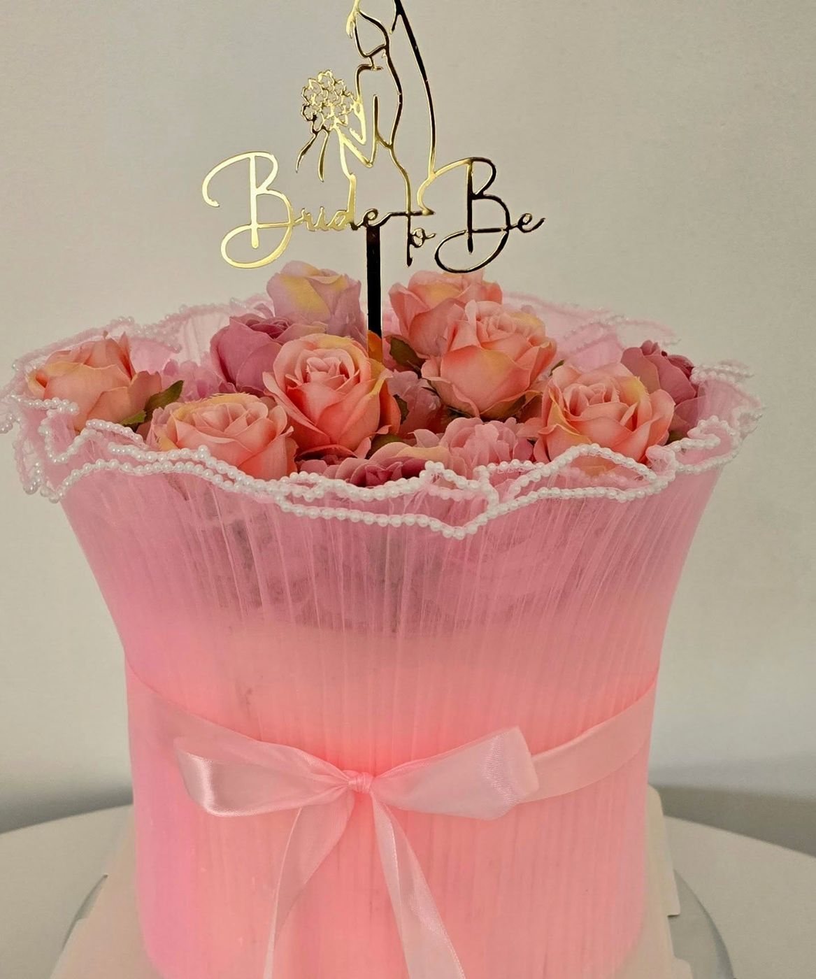 A tall pink celebration cake dressed with fresh roses