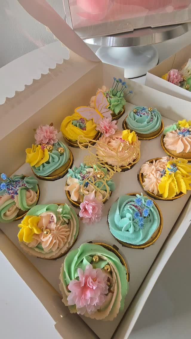 A box of pastel cupcakes with buttercream swirls and flowers